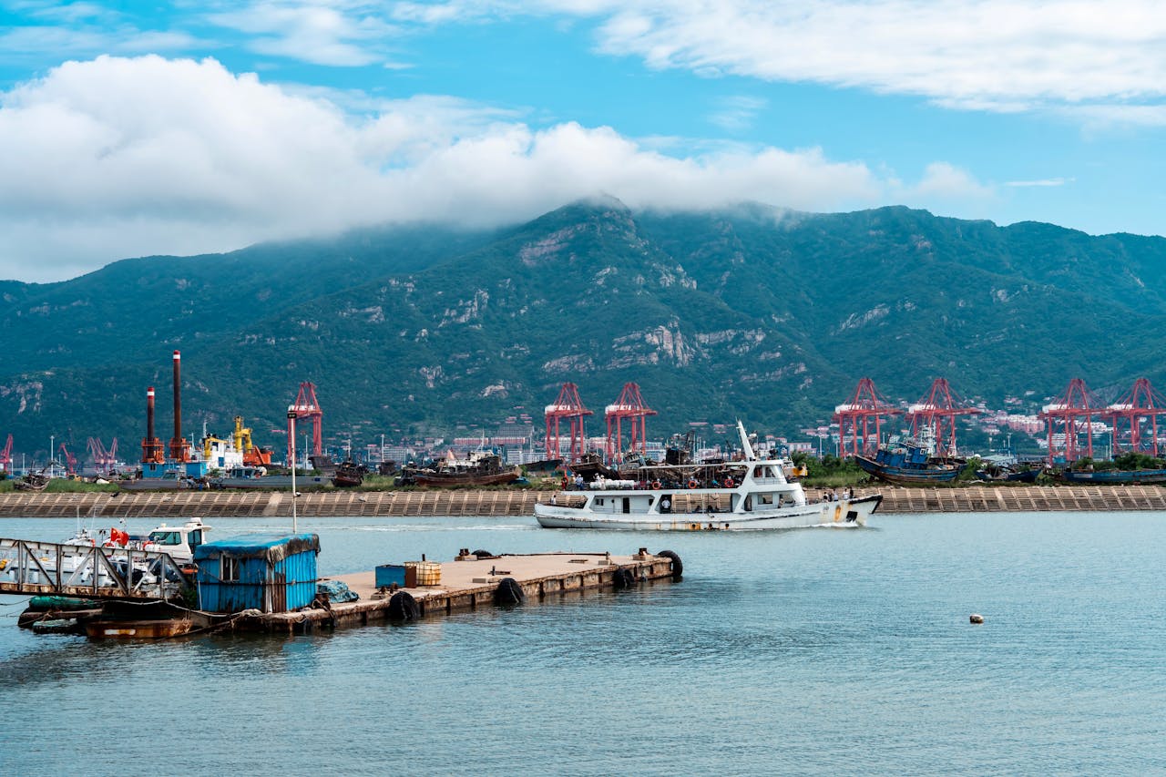 A bustling port scene with cranes, boats, and mountains under a clear sky.